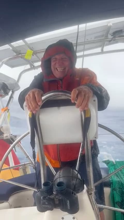 Gerhard Hoffmann at the helm of a sailing yacht in foul-weather gear, grinning, with spray across the cockpit